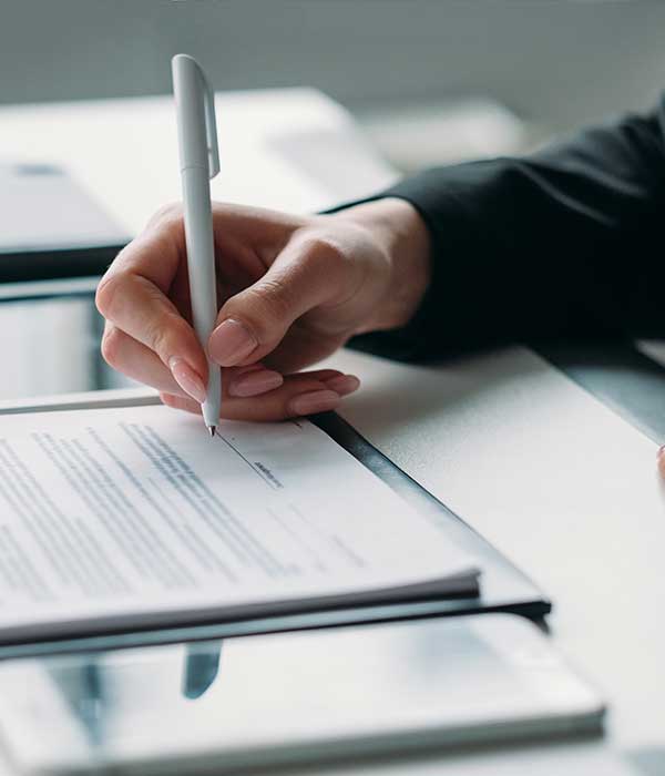 Image of a hand holding a pen, signing a contract of some kind.